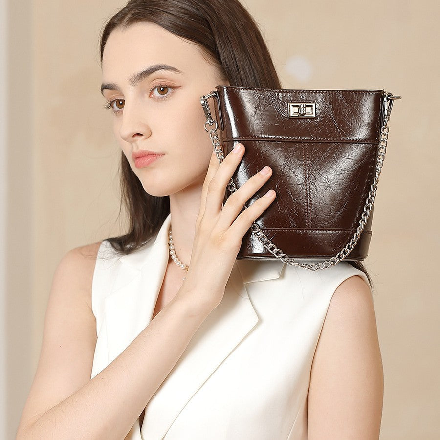 Woman holding a brown leather handbag with a chain strap against a beige background