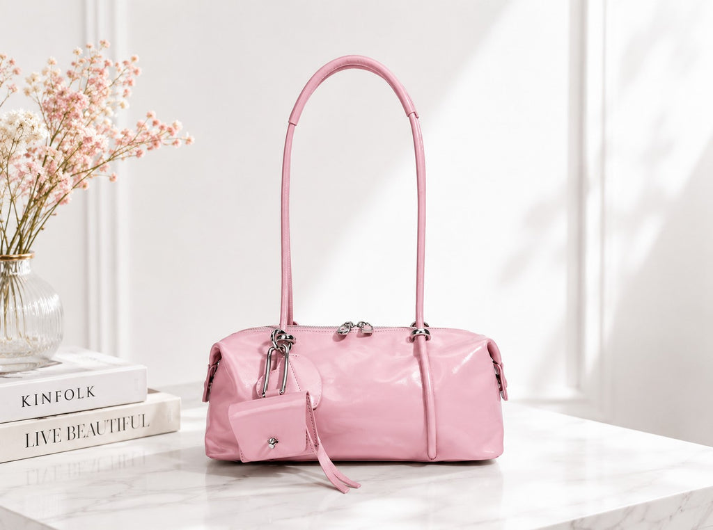 Pink handbag on a white surface with books and flowers in the background