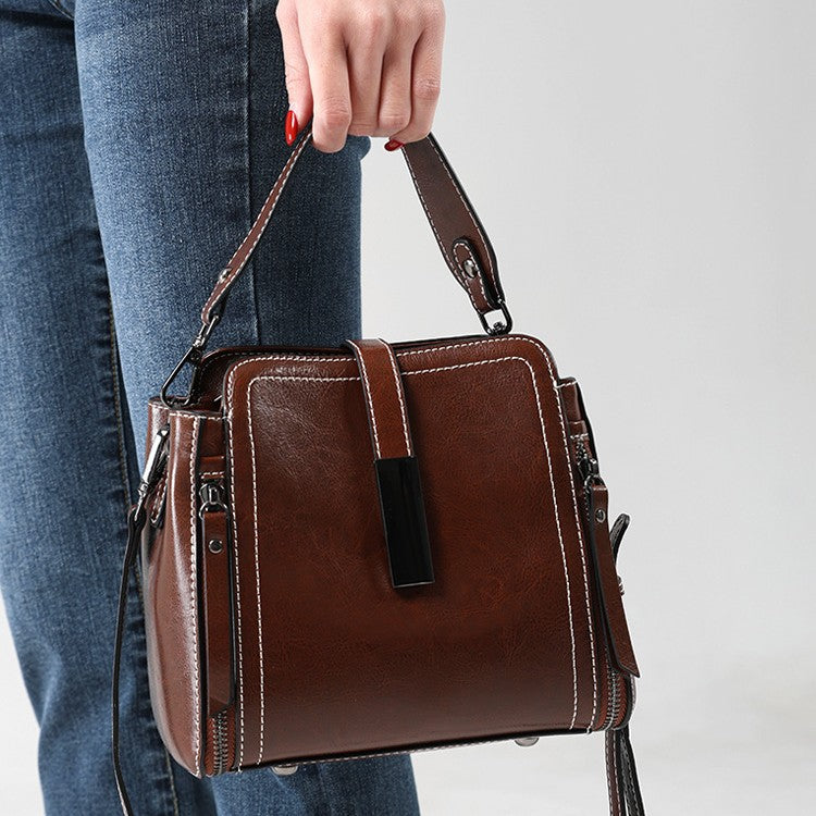 Brown leather handbag held by a person wearing blue jeans on a light gray background