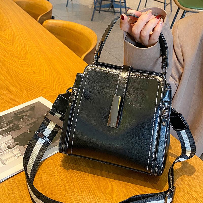 Black handbag with striped strap on a wooden table, person holding it.