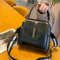 Black handbag with striped strap on a wooden table, person holding it.