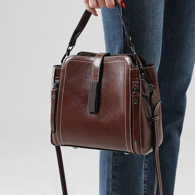 Brown leather handbag held by a person wearing blue jeans on a light gray background