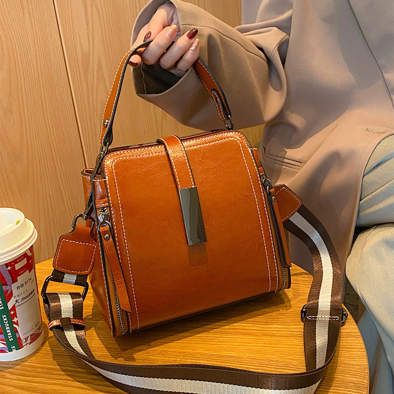 Brown handbag with a strap held by a person on a wooden surface.