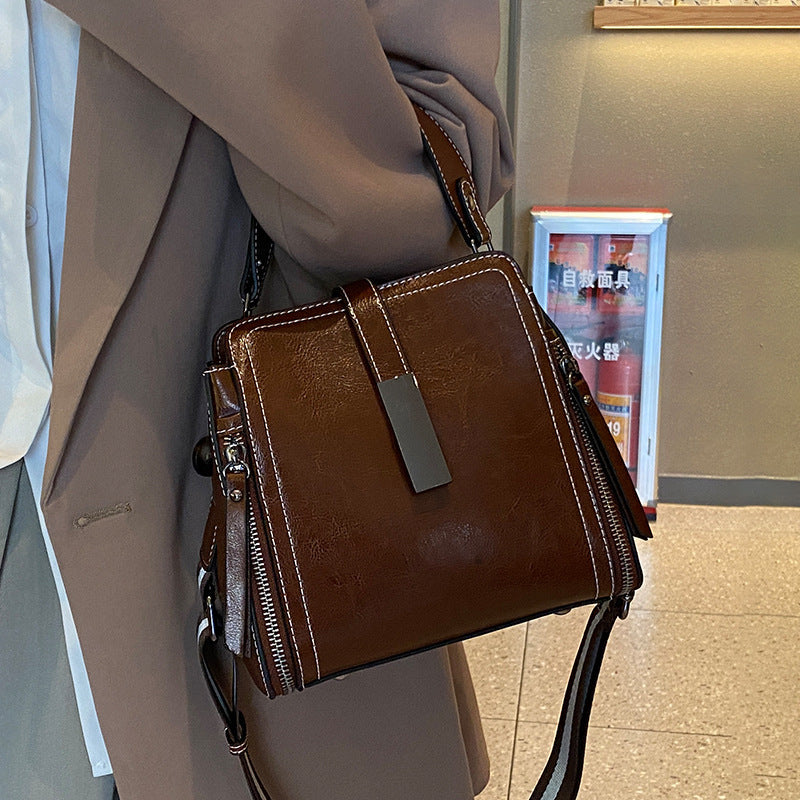 Brown leather handbag held by a person wearing a coat indoors.