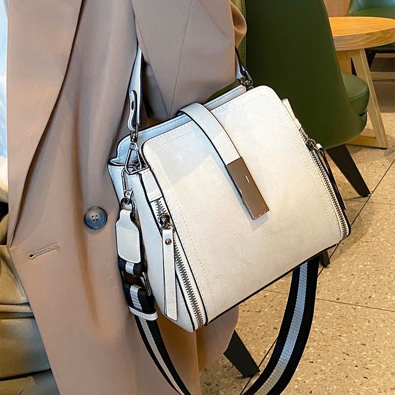 White handbag with black strap held by a person wearing a beige coat.