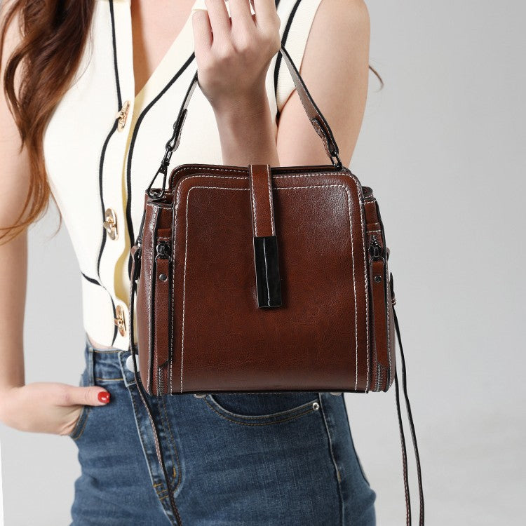 Brown leather handbag held by a person against a neutral background