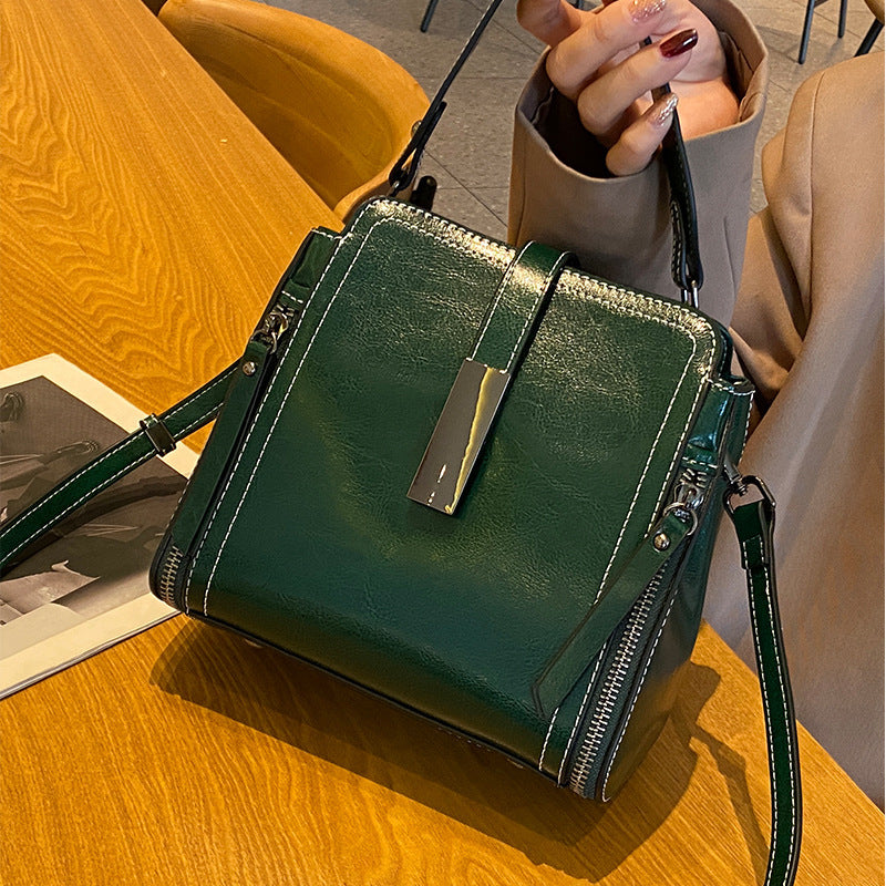 Green handbag on a wooden surface with a person holding it.