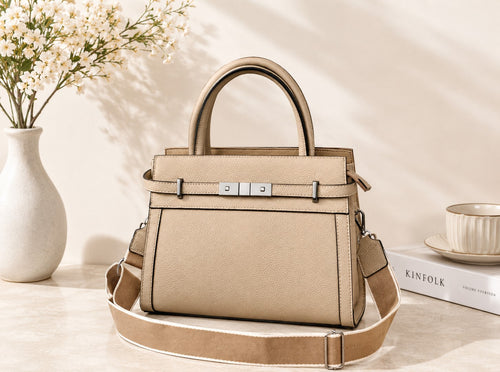 Beige handbag on a light surface with a vase of flowers and books in the background