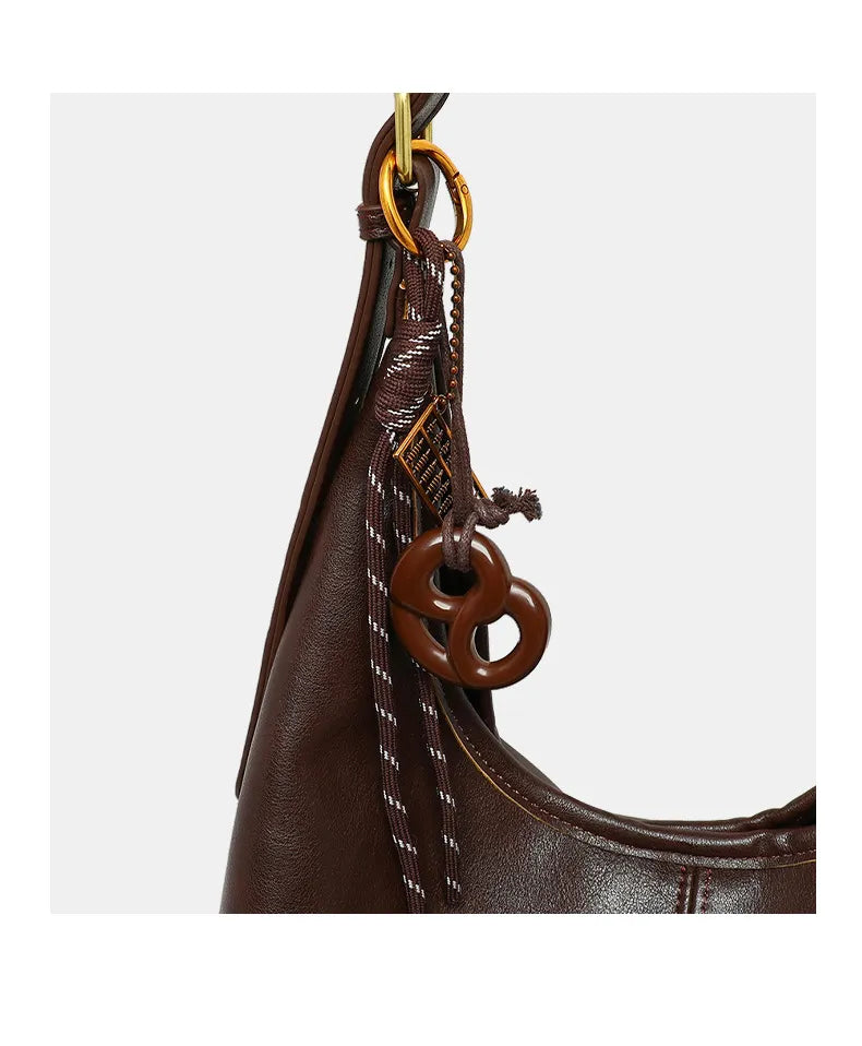 Brown leather handbag with decorative keychain on a white background