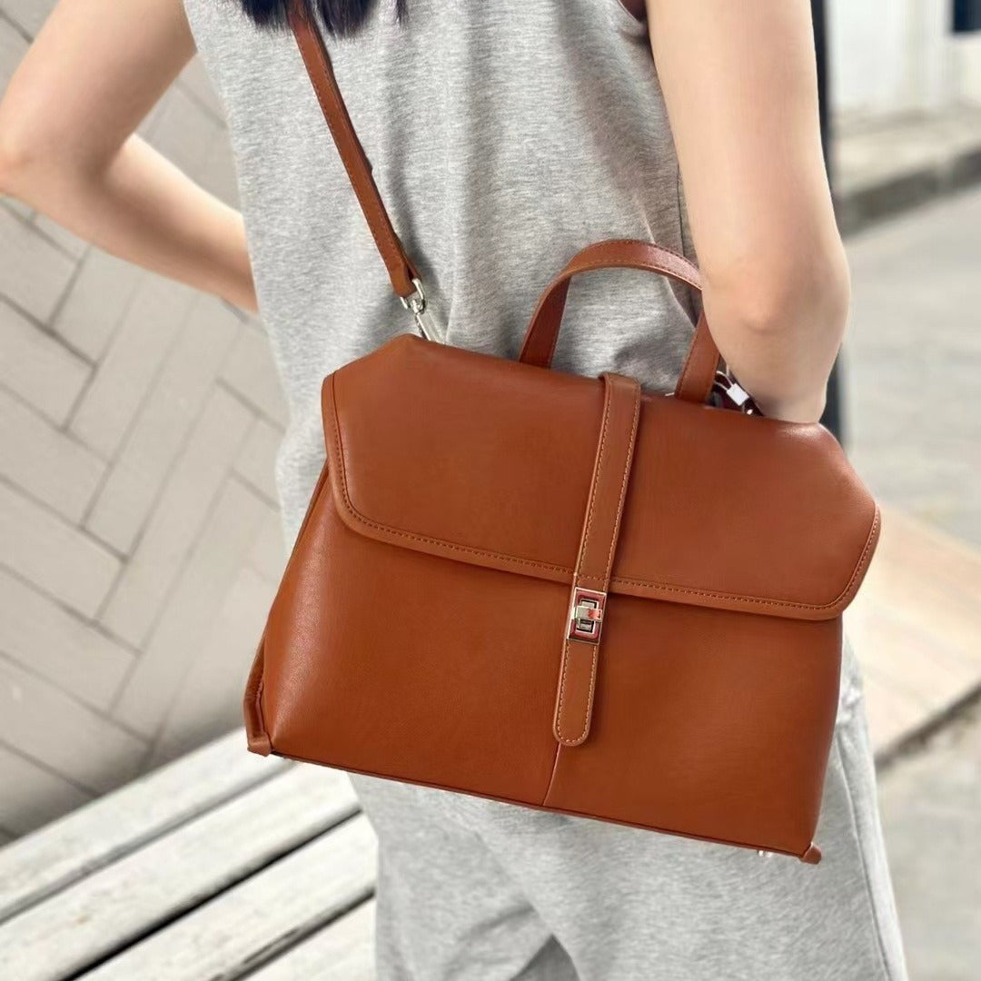 Brown leather handbag carried by a person on a blurred background