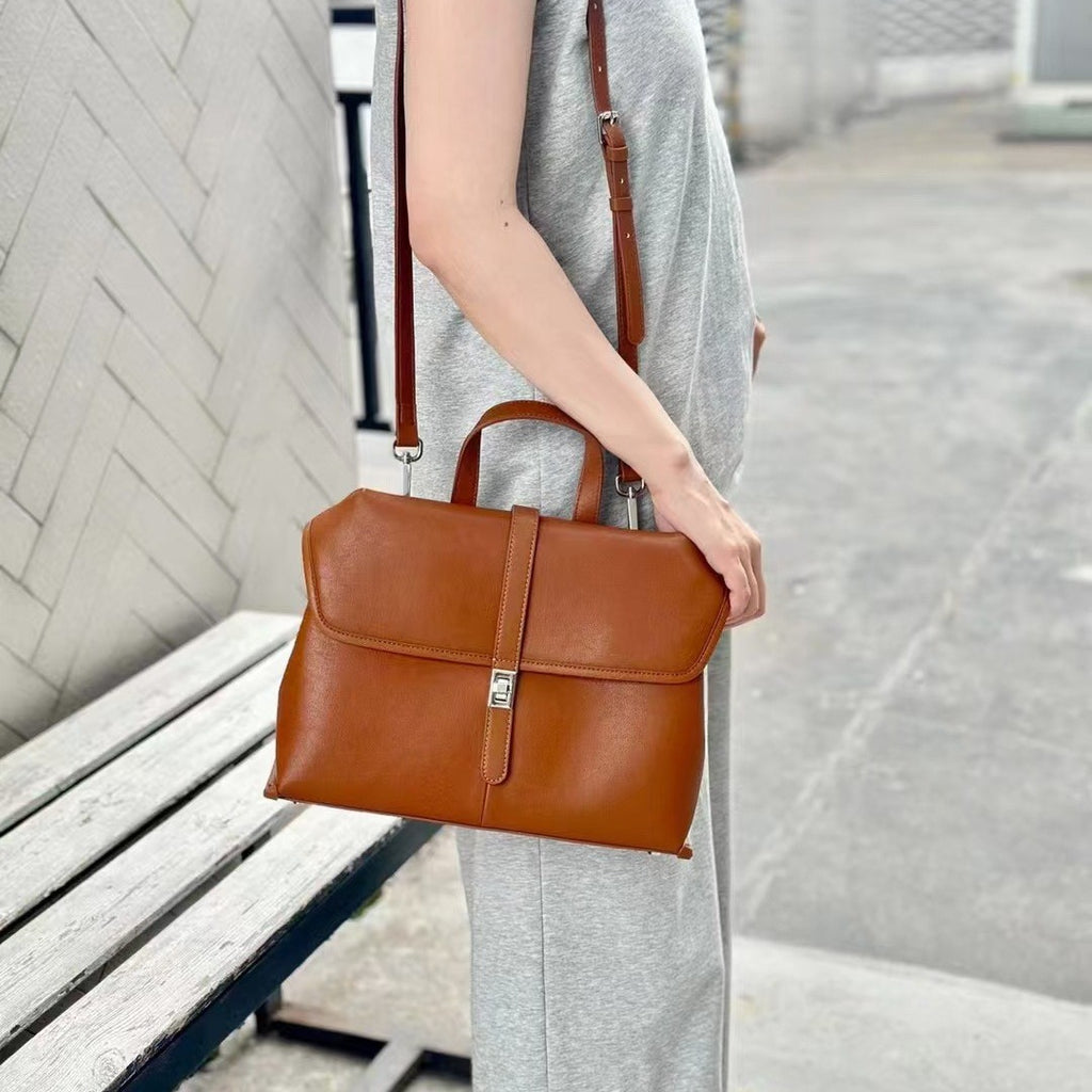 Person holding a brown leather handbag in an urban setting