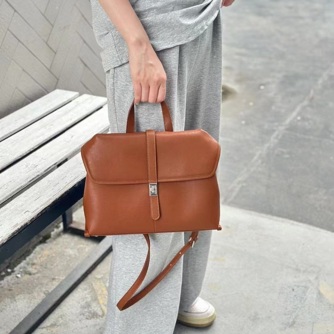 Person holding a brown leather bag on a sidewalk