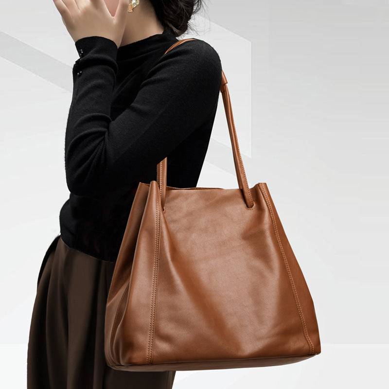 Person holding a brown leather handbag against a white background