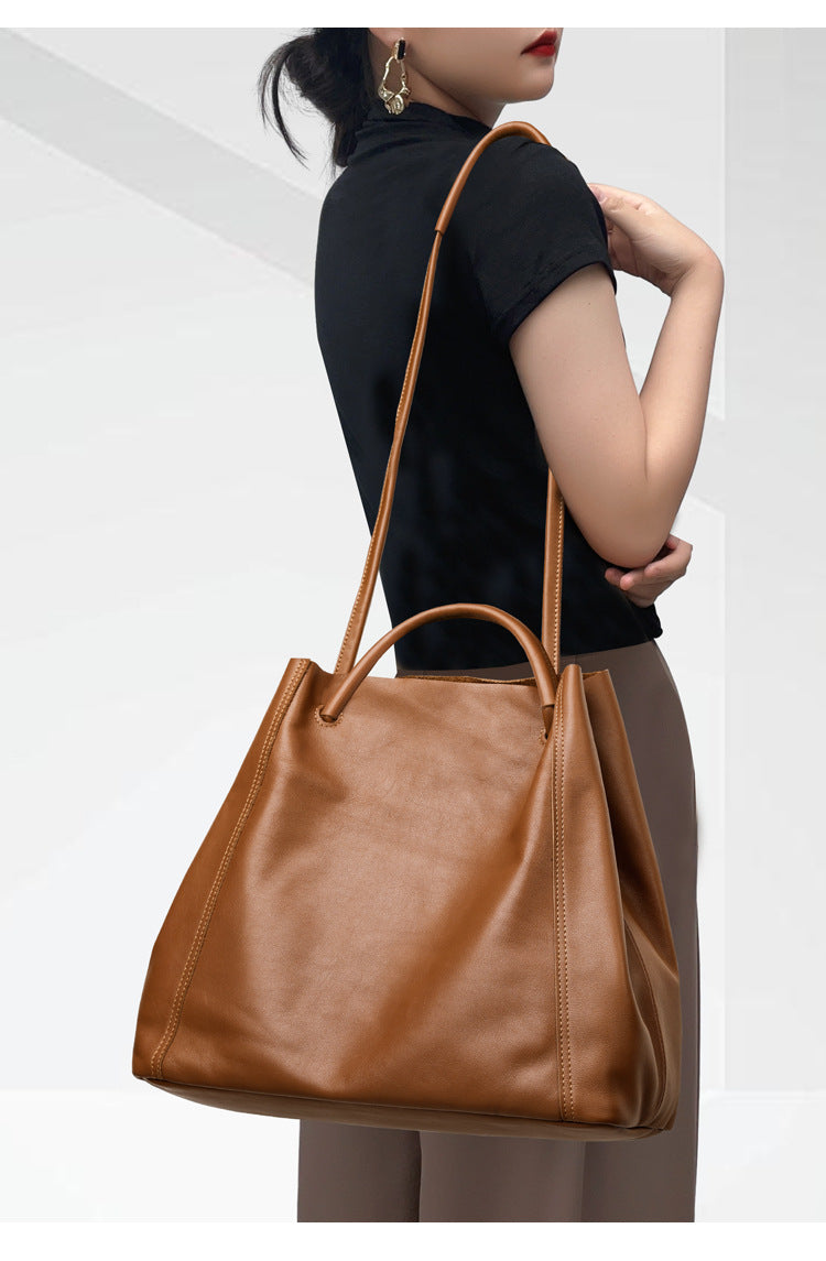 Person holding a brown leather handbag against a plain background