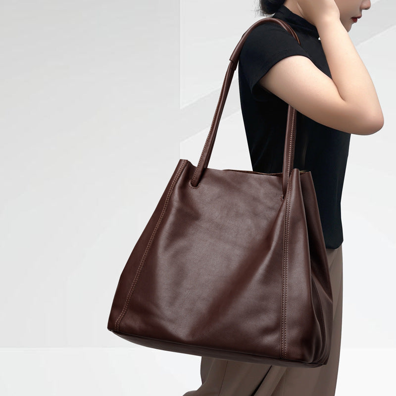 Person holding a brown leather handbag against a white background