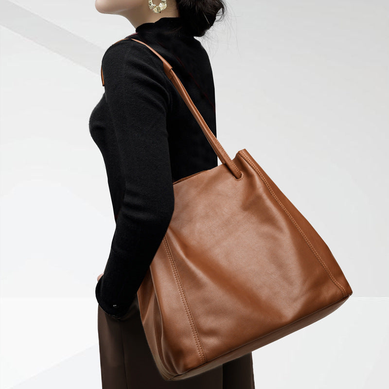Brown leather handbag held by a person wearing a black turtleneck against a white background