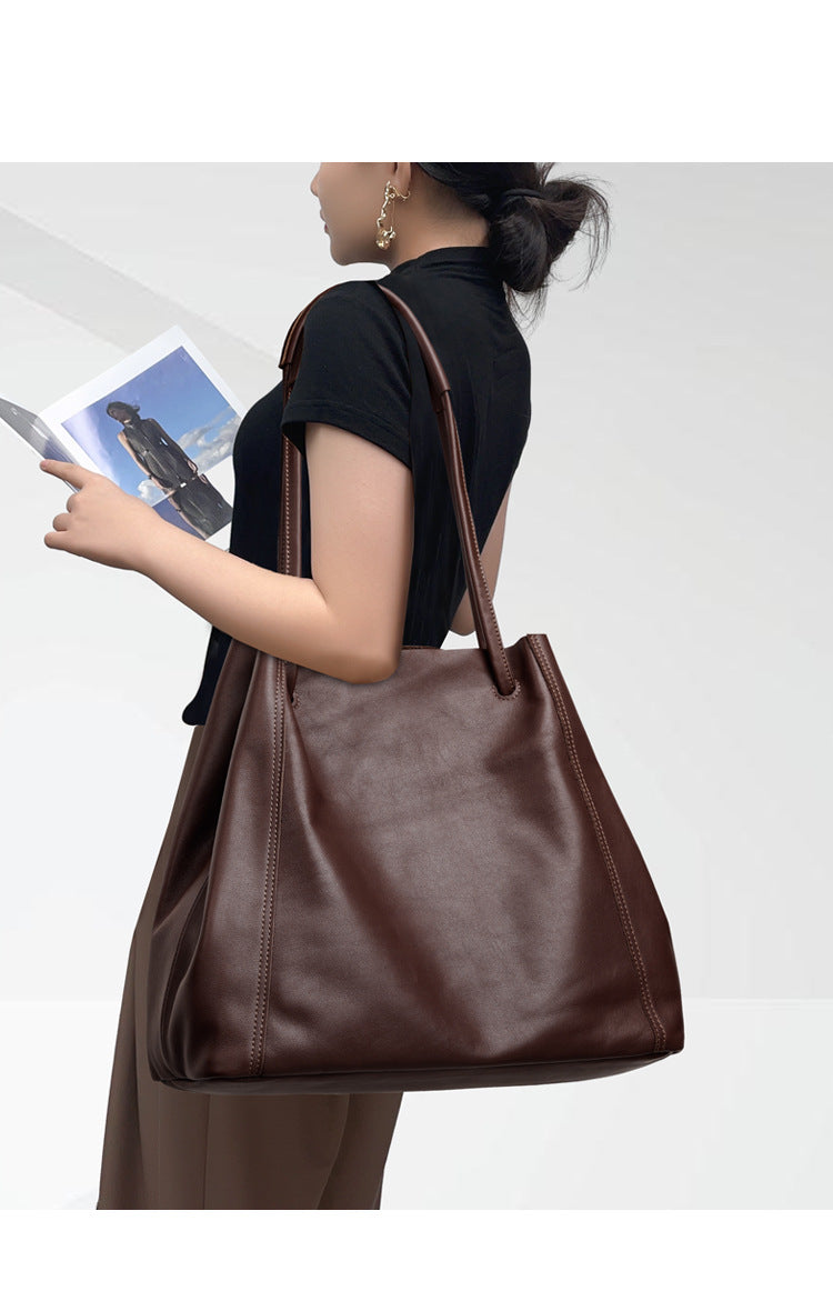 Person holding a brown leather tote bag with a white background