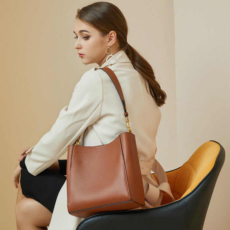 Woman holding a brown leather handbag sitting on a chair with a beige background