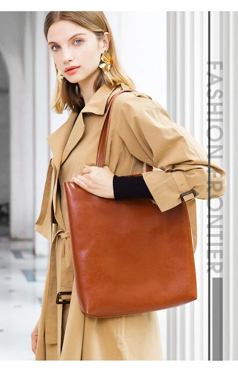 Woman holding a brown leather tote bag in front of a blurred indoor background