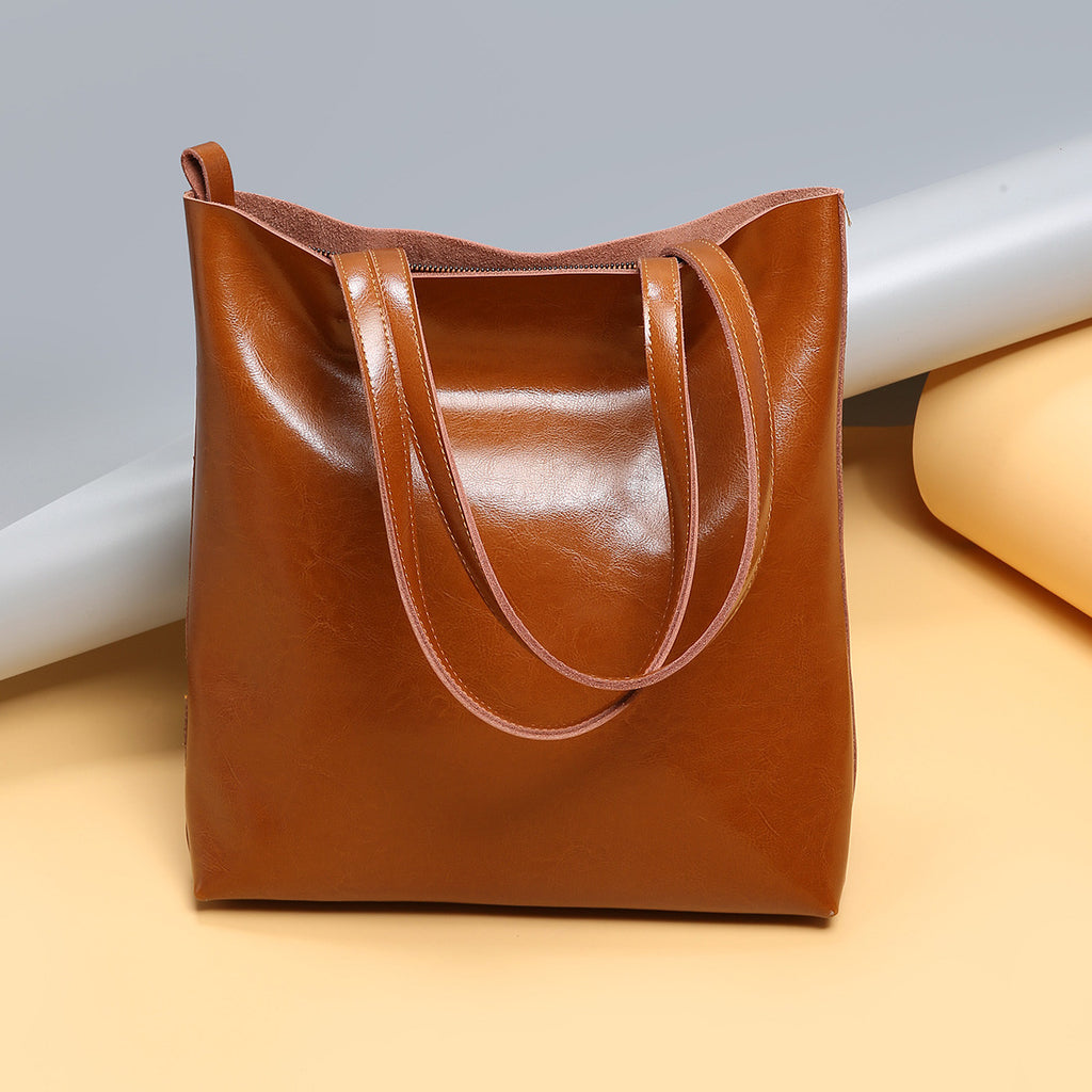 Brown leather tote bag on a light beige surface with a gray background