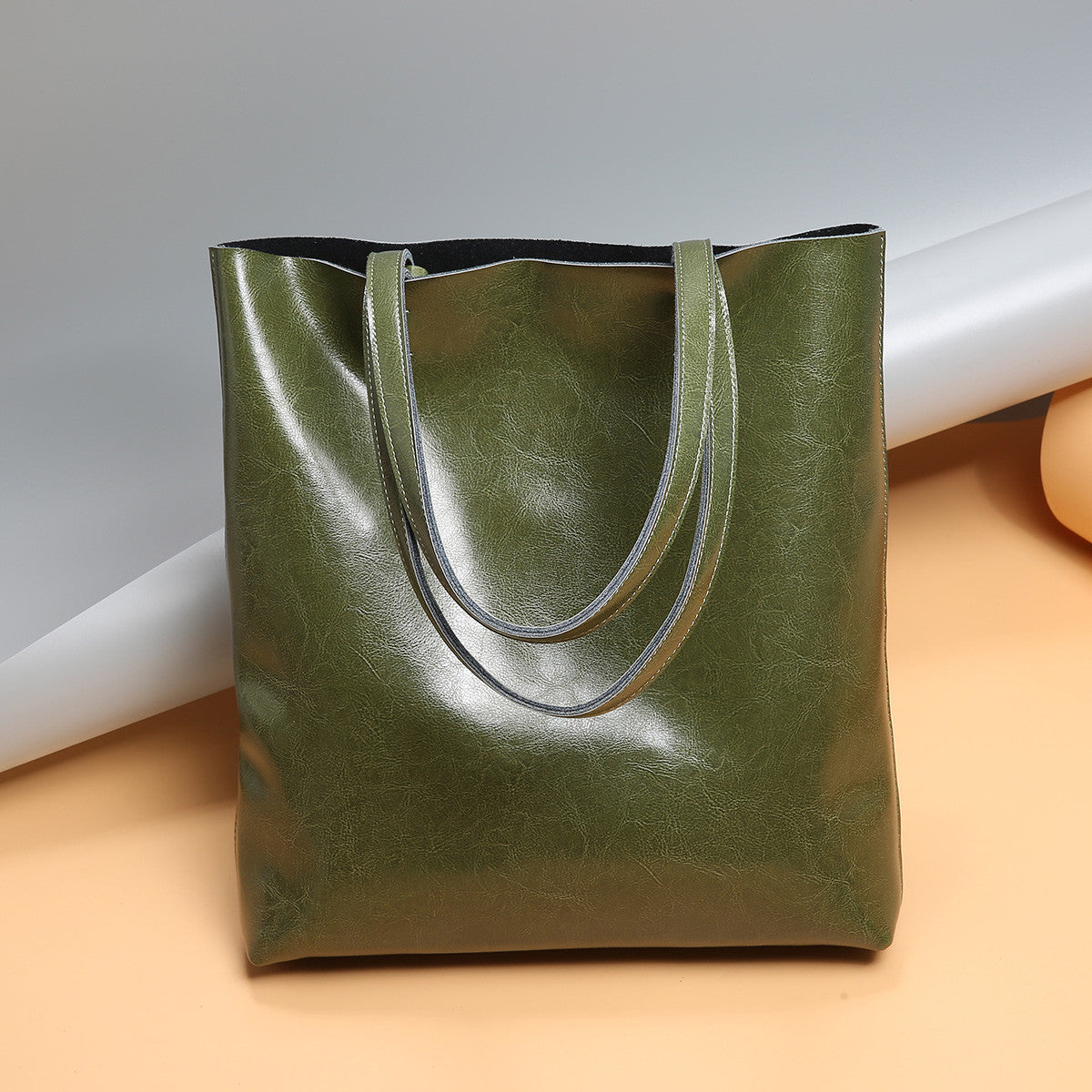 Green leather tote bag on a light brown surface with a white background